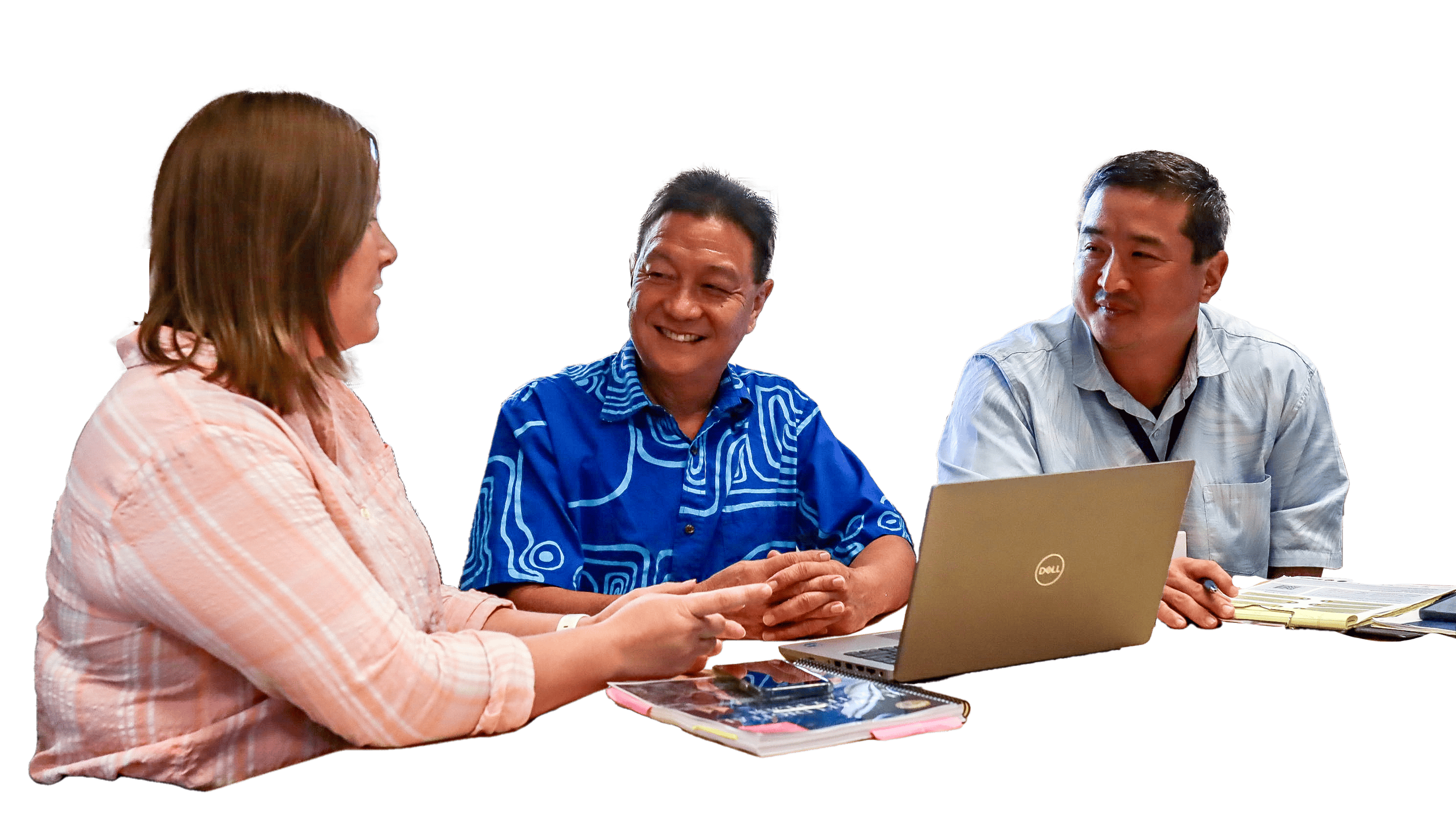 Three individuals are seated at a table having a discussion. One person is using a laptop, while another has books and notebooks in front of them. They appear to be engaged and smiling, suggesting a collaborative and friendly conversation. The background is transparent.