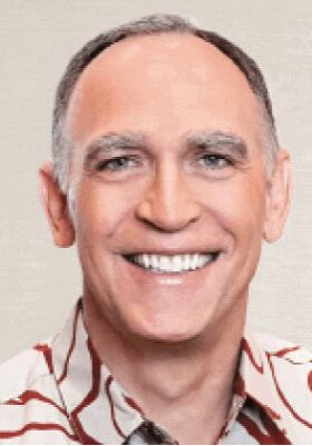 A person with short hair and a friendly smile, wearing a patterned button-up shirt, photographed against a plain background.